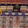 A colorful board game layout with intricate patterns and game pieces. The board features rows and columns with different symbols and tracks, including small structures resembling buildings and pawn-like figures in blue, red, and yellow.